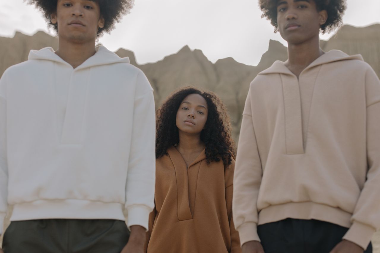 Home Three young adults pose stylishly outdoors against a natural backdrop, showcasing modern fashion.