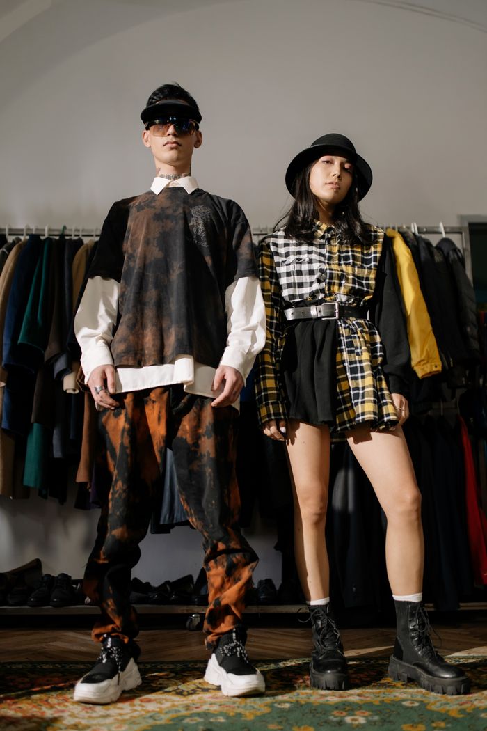 Home Two individuals pose confidently in a vintage clothing store showcasing urban fashion style.