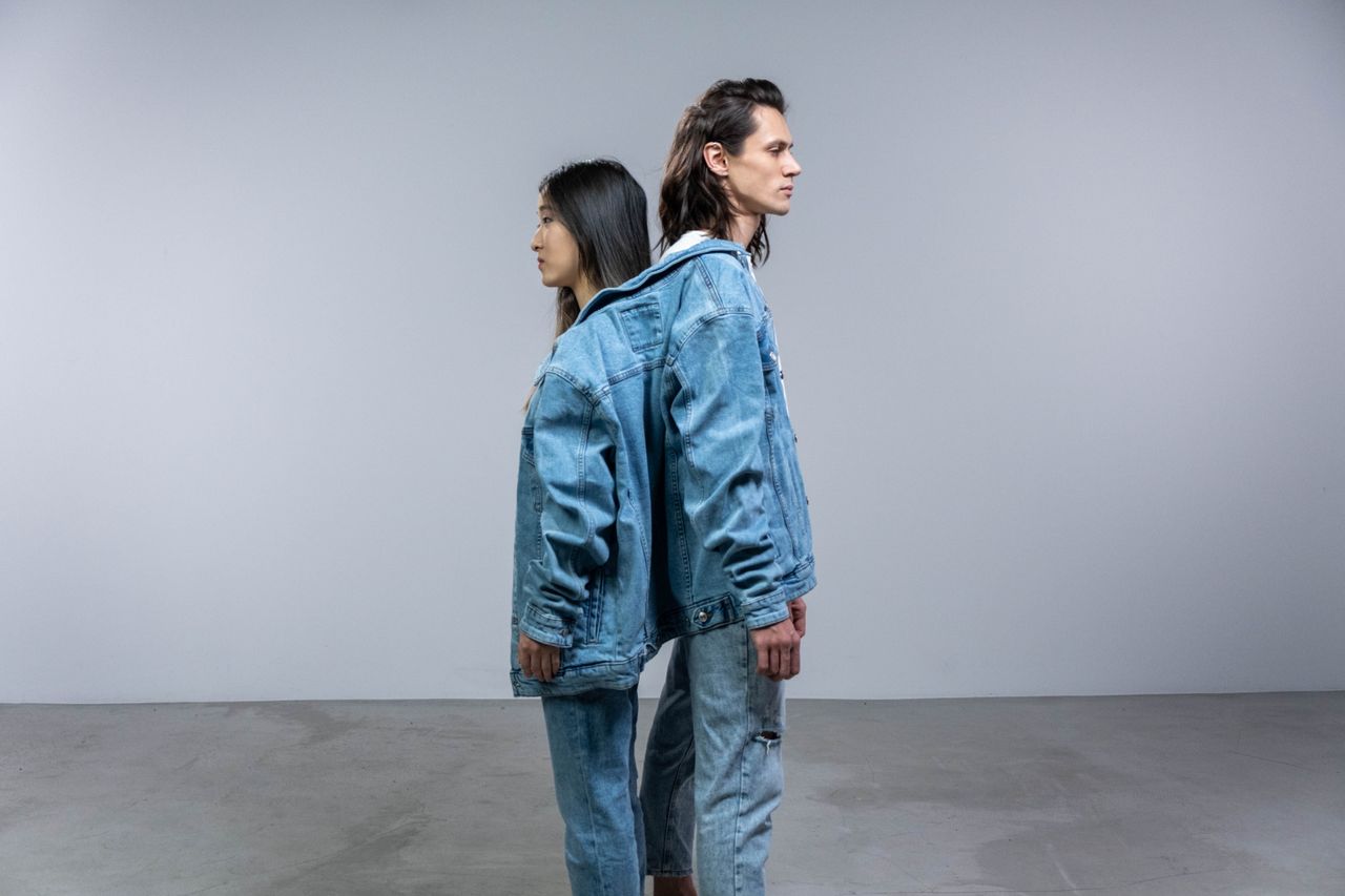Home Two models in denim jackets and jeans standing back-to-back. Modern fashion style.