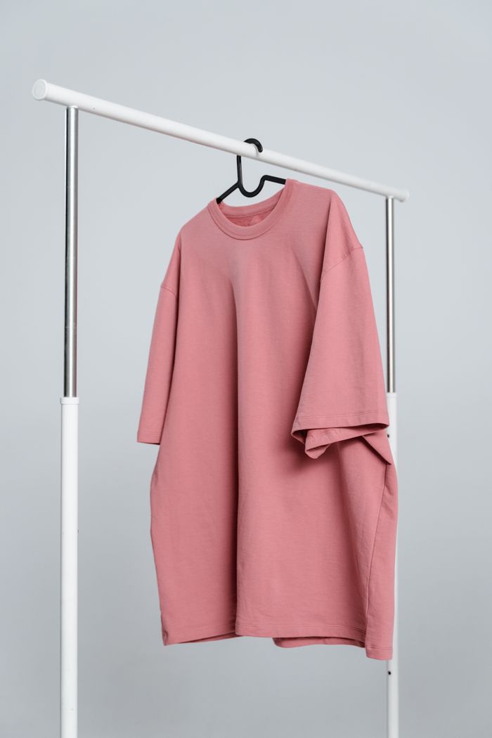 Home A minimalist pink unisex t-shirt hanging on a white rack against a light background.